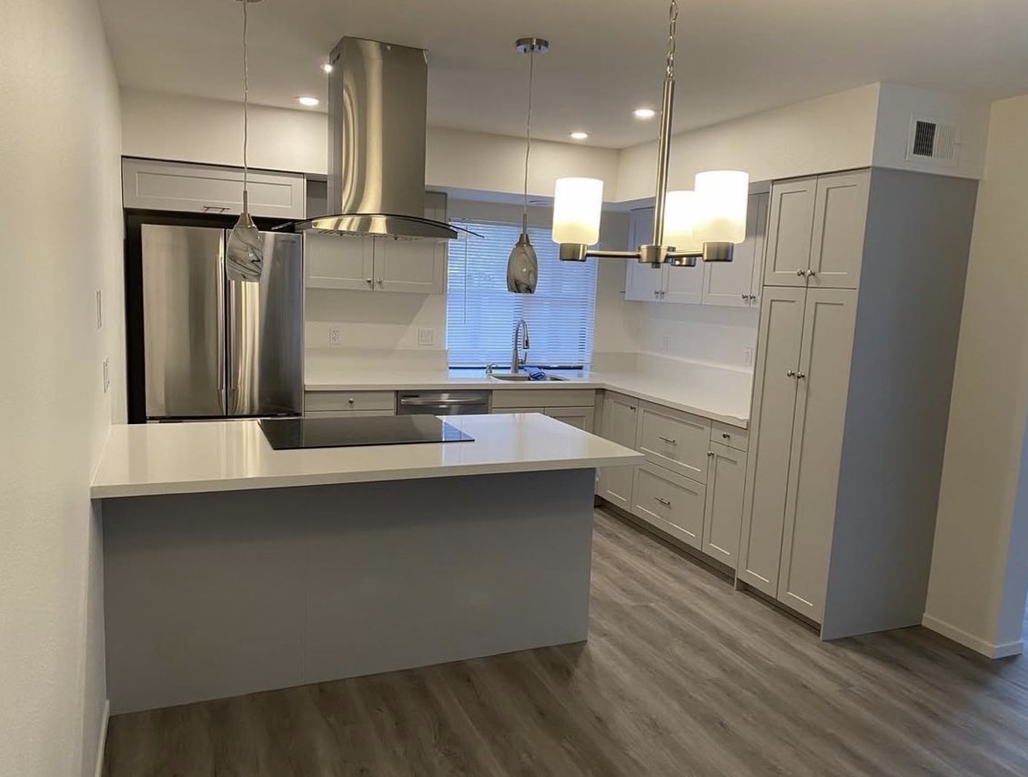 Remodeled kitchen with gray shaker cabinets, white counters, a peninsula with cooktop and stainless range hood